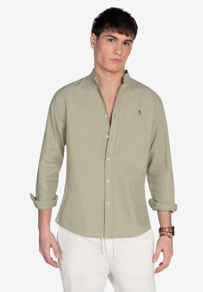 Camisa de botones verde claro con mangas largas, puños enrollables y una textura sutil. Presenta un pequeño diseño bordado en el pecho.