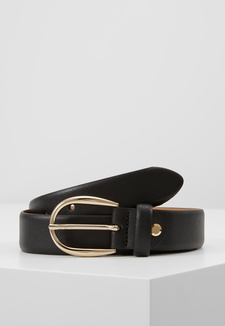 Ceinture en cuir noir texturé avec boucle dorée brillante et arrondie reposant sur une surface blanche sur fond gris clair.
