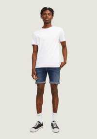 Camiseta blanca de cuello redondo, pantalones cortos de mezclilla azul con puños doblados y zapatillas negras con suelas blancas. Un atuendo simple y casual de verano.