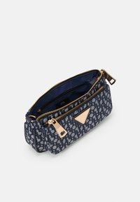 Tmavě modrá vzorovaná kabelka s kultivovanými zlatými zipy, otevřenou hlavní kapsou, přední kapsou na zip a trojúhelníkovou zlatou kovovou štítkem značky.