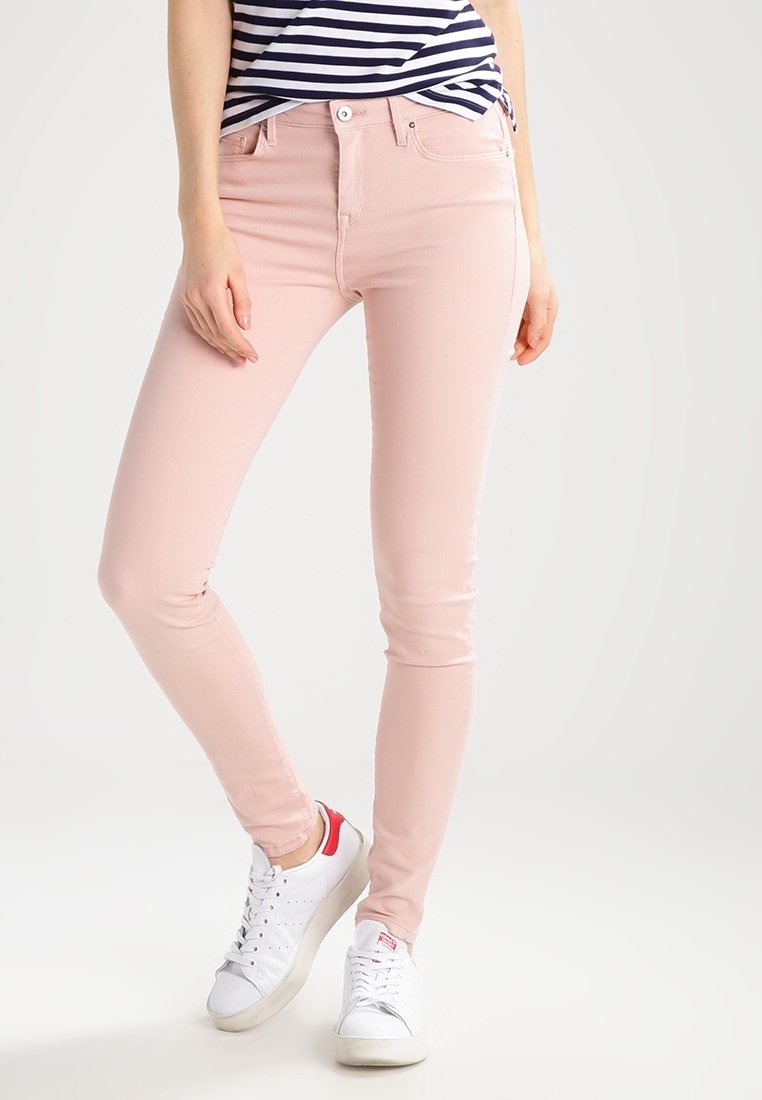 Jeans ajustados de color rosa claro, hechos de una mezcla de algodón elástica, que cuentan con un diseño clásico de cinco bolsillos y costuras sutiles. Llevados con zapatillas blancas.