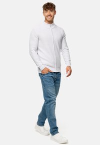 Sudadera de cremallera gris claro con cuello alto, combinada con vaqueros azules y zapatillas blancas. Enfóquense en la textura de la tela y el ajuste casual.