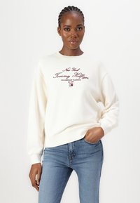 Krémová mikina s okrúhlym výstrihom a dlhými rukávmi, so vyšívaným textom v bordovej farbe "New York Tommy Hilfiger" a malým logom.