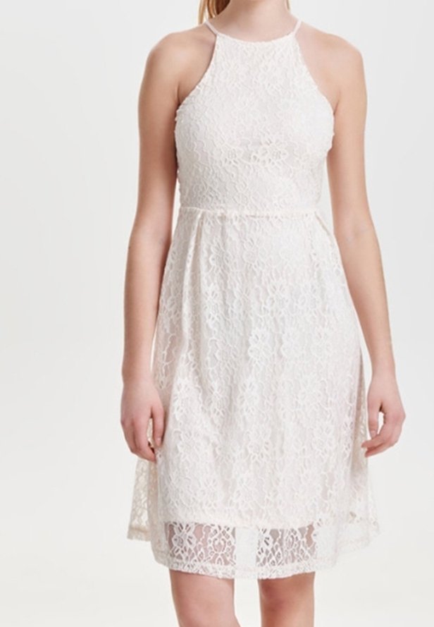 Valkoinen pitsimekko, jossa on halterneck-olkaimet, tiukka yläosa ja levenevä helma. Kankaan pinnassa on kukkakuvioita ja läpinäkyvä päällyste.