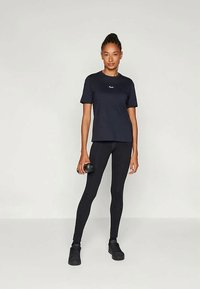 Marineblå sports T-shirt og sorte leggings, tætsiddende design, letvægtsstof, model holder en sort håndvægt, står på ensfarvet baggrund.