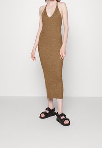 Brun stickad halterklänning med en åtsittande silhuett, med V-ringning och sideslits. Matchad med svarta texturerade sandaler.