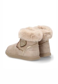 Botines de ante beige claro con un suave cuello de piel, un adorno en forma de corazón dorado y detalles texturizados. Suela de goma resistente para mayor soporte.