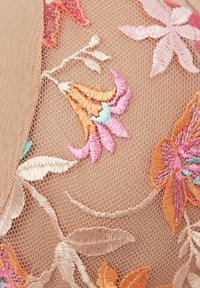 Borduurstof in beige toont kleurrijke bloempatronen in roze, oranje en blauw, met fijne details en een zachte textuur.