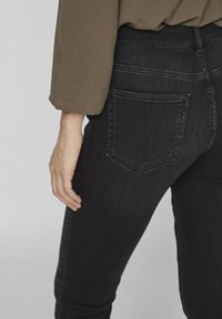 Jeans de mezclilla negra con corte slim, que cuentan con bolsillos traseros y un sutil efecto de desgaste. El material parece suave con una textura ligeramente cepillada.