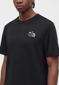 Άνδρας που φοράει μαύρο κοντομάνικο T-shirt με μικρό λευκό λογότυπο The North Face στο αριστερό στήθος.