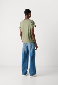 Olivgrünes, tailliertes T-Shirt mit kurzen Ärmeln, kombiniert mit hellblauen, weit geschnittenen Jeans, getragen mit cremefarbenen Sneakers.
