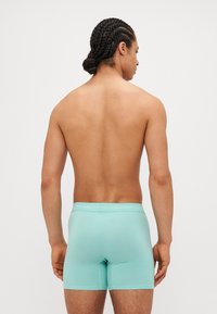Boxeri din bumbac de culoare albastru deschis cu un ciorap moale, având logo-ul Calvin Klein, văzuți din spate pe un fundal simplu.