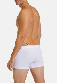 White cotton boxer shorts with a fitted design, flat waistband, and smooth texture, worn by a shirtless man showing his side profile.
