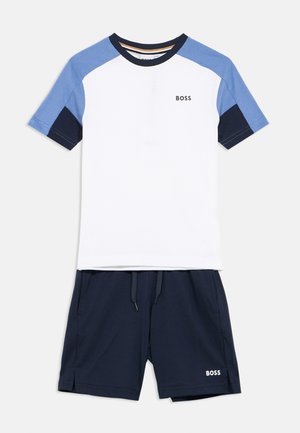 Bela majica kratkih rokavov z modrimi in mornarsko modrimi poudarki ter logotipom "BOSS". Kombinirana z mornarsko modrimi kratkimi hlačami, prav tako z logotipom na strani.