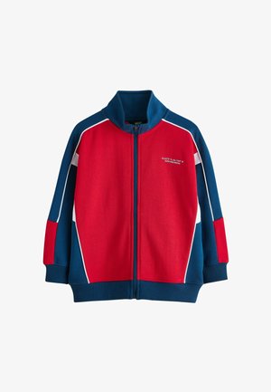 Lasten vetoketjullinen takki, jossa punainen etuosa, siniset hihat ja kaulus, valkoiset reunat sekä vasemmassa rinnassa pieni valkoinen teksti.