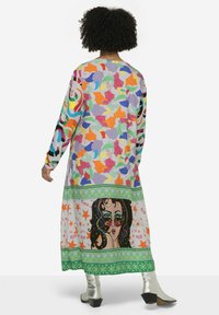 Langes, farbenfrohes Kleid mit einem gemischten Muster aus abstrakten Formen und einem grafischen Druck eines Frauenporträts am unteren Rand; lange Ärmel und ein runder Ausschnitt.