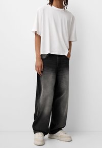 Bílý bavlněný tričko s volným střihem, spárované s širokými černými džíny se stupňující texturou a krémovými teniskami.