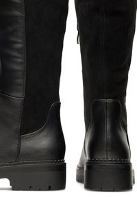 Botas negras de tobillo que combinan cuero liso y ante, con un característico tacón apilado y detalles de costura visibles.