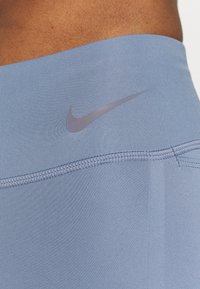 Jasnoniebieski, sportowy pas z logo Nike w kolorze srebrnym, wykonany z elastycznej tkaniny o gładkiej fakturze i subtelnym wzorze prążkowym.