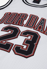 Λευκή μπασκετική φανέλα από δίχτυ με μαύρα και κόκκινα κεντημένα γράμματα "JORDAN" και τον αριθμό "23". Σχέδιο με διπλή ρίγα στο λαιμό σε στυλ crew neck.