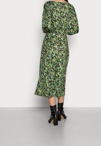 Kukallinen mekko mustalla pohjalla, jossa on vihreitä lehtiä. Keskipitkä, rento malli ja puffihihat, yhdistetty mustiin korkokenkiin.
