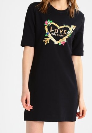Robe noire à manches courtes avec un cadre en bois en forme de cœur et une broderie florale autour des mots "Love Moschino" sur la poitrine.