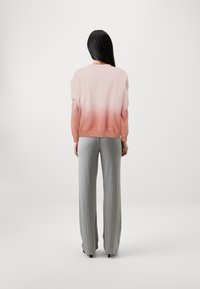 Felpa rosa chiaro con un effetto sfumato che va dal rosa pallido al pesca scuro, abbinata a pantaloni grigi a coste a gamba larga. Design morbido e casual.