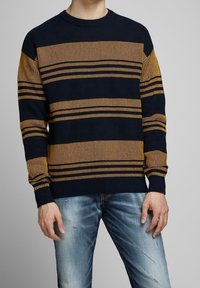 Marinblå och senapsgul randig stickad tröja med rund halsringning och ribbade ärmslut, ihop med ljusblå slitna jeans.