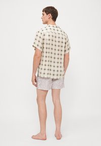 Camicia a maniche corte a scacchi color crema con quadrati neri, abbinata a pantaloni corti grigi chiari con una stampa logo discreta.