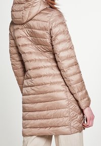 Beige pufferjack met capuchon, voorzien van een horizontaal gestikte ontwerp, een gladde glanzende afwerking en details aan de zijnaad. Half lange stijl.