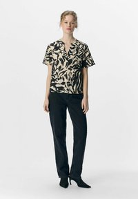 Kortærmet bluse i beige med sort abstrakt print, med en notch-udskæring. Sammen med sorte højtaljede jeans og spidse sko.