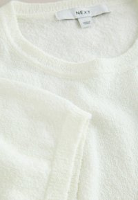 Haut blanc texturé en éponge à manches courtes avec encolure ronde et manches repliées, montrant l'étiquette de la marque Next à l'intérieur du col.