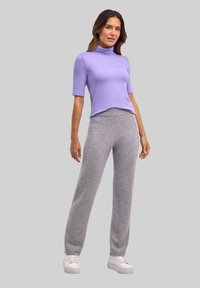 Lichtpaarse korte mouwen coltrui gecombineerd met grijze wijde broek. Model draagt witte sneakers en staat tegen een grijze achtergrond.