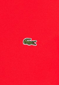Rode polo shirt met een klein groen geborduurd krokodil logo. De stof heeft een gestructureerde weving en een opvallende kraag.