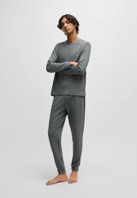 Grijze loungewear set bestaande uit een langemouwen top en taps toelopende broek, gemaakt van textuurstof met subtiele patronen.