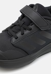 Chaussure de sport noire avec tige en tissu en maille, revêtements synthétiques, sangle réglable et semelle en caoutchouc avec accents texturés.