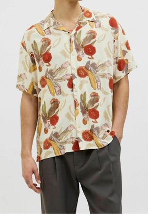 Chemise crème à manches courtes avec un motif floral abstrait coloré, portée avec un pantalon plissé gris foncé.