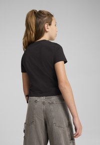 Camiseta de algodón negra con mangas cortas y un diseño recortado. Combinada con pantalones cargo gris claro que cuentan con bolsillos pronunciados y un acabado texturizado.