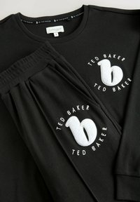 Top lungo a maniche nere a costine abbinato a pantaloni, con loghi ricamati bianchi e finitura testurizzata. Vita elasticizzata sui pantaloni.