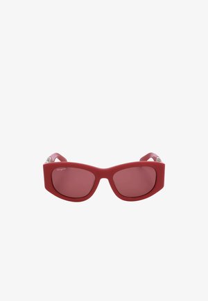 Occhiali da sole rossi a forma di occhio di gatto con montatura spessa e lenti colorate, con un logo discreto nell'angolo in alto a sinistra della lente.