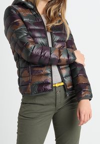 Puffjakke i mørkegrøn og brun camouflage mønster, med hætte, lynlås og quiltet overflade. Matchende med olivengrønne bukser og en grå top.