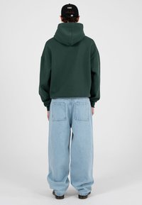 Roheline kapuutsiga dressipluus, millel on mugav lõige, kombineeritud helesiniste laiade pükstega. Sile tekstuur nähtavate õmblustega ja kaks tagataskut.