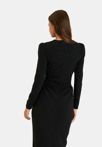 Schwarz, langärmliges Kleid mit figurbetontem Schnitt, strukturiertem Stoff, dezenten Strassdetails und gerafftem Design an der Taille.