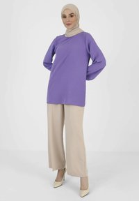 Lilac long-sleeve tunic with a V-neck, paired with beige wide-leg trousers and light-colored heels. Smooth fabric with a relaxed fit.