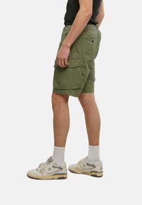 Shorts cargo verts en coton avec plusieurs poches, une coupe décontractée et une taille avec cordon de serrage. Assortis avec des baskets légères.