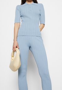 Haut en tricot côtelé bleu clair à manches courtes avec trois boutons au col, associé à un pantalon ajusté assorti ; un sac à main crème complète l'ensemble.