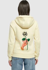 Felpa gialla con una grafica di una mano che tiene una rosa bianca, con foglie verdi. Tessuto morbido e vestibilità rilassata con cappuccio.