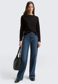 Zwart gebreid sweater met een ronde hals, gecombineerd met hoge taille, wijde blauwe denim jeans. Geaccentueerd met een zwarte schoudertas.