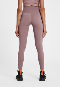 Leggings in een zachte mauve kleur met een hoge tailleband, een textuurpatroon en gecombineerd met zwarte laarzen met een oranje accent.
