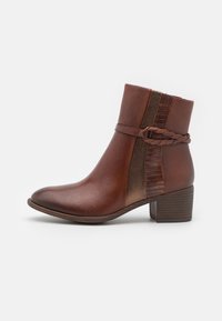 Bottine en cuir marron avec un bout effilé, des panneaux latéraux texturés, un accent en sangle tressée et un petit talon empilé. Fini lisse.